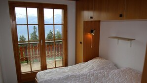 A bedroom with a bed, a wooden door, a small shelf, and a view of mountains through a glass door. - Extravagant Apartment With View (Sion)