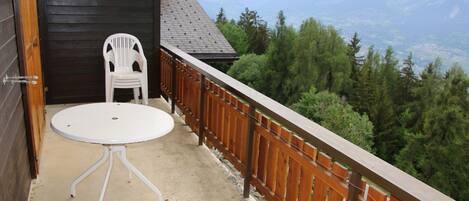 Un balcon avec une table et des chaises blanches, une clôture en bois et une vue sur la montagne.