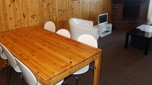 A wooden-paneled room with a wooden dining table, white chairs, a white sofa, a television, and a fireplace. - Apartment With Mountain Views (Sion)