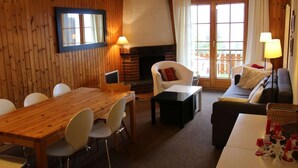 A cozy living room with a wooden dining table, white chairs, a sofa, and a fireplace. - Apartment With Mountain Views (Sion)