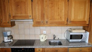 A kitchen with wooden cabinets, a built-in dishwasher, a coffee maker, a kettle, and a microwave. - Authentic Apartment With Mountain Views (Veysonnaz)