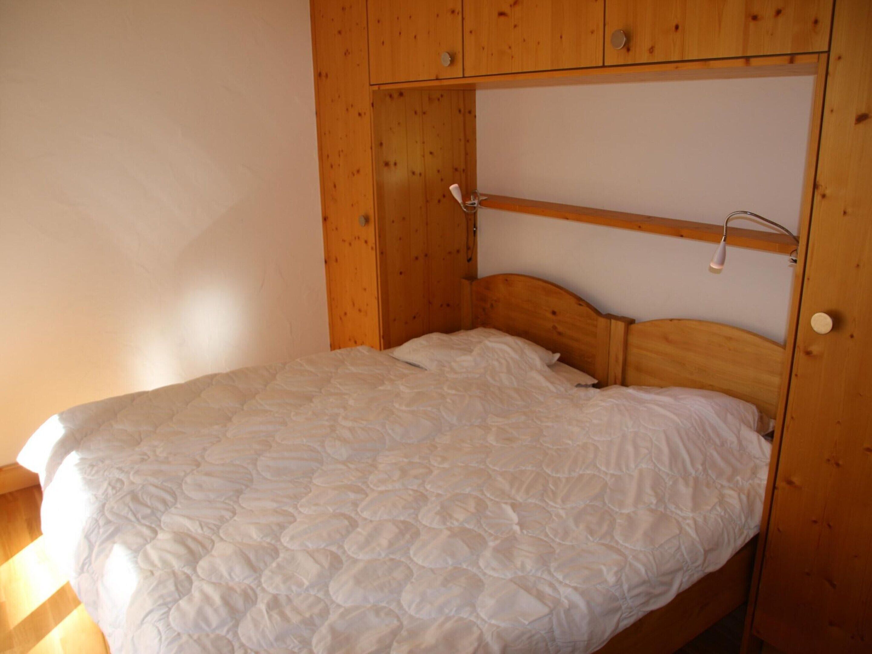 A single bed with a quilted white duvet in a room with wooden walls and a slanted ceiling.
