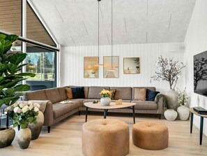 Una sala moderna con un sofá modular, una mesa de centro redonda y otomanas.