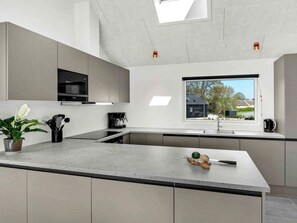 A modern kitchen with a large island, built-in appliances, and a window offering a view of the outside. - 5 Star Holiday Home in Dronningmolle (Dronningmolle)