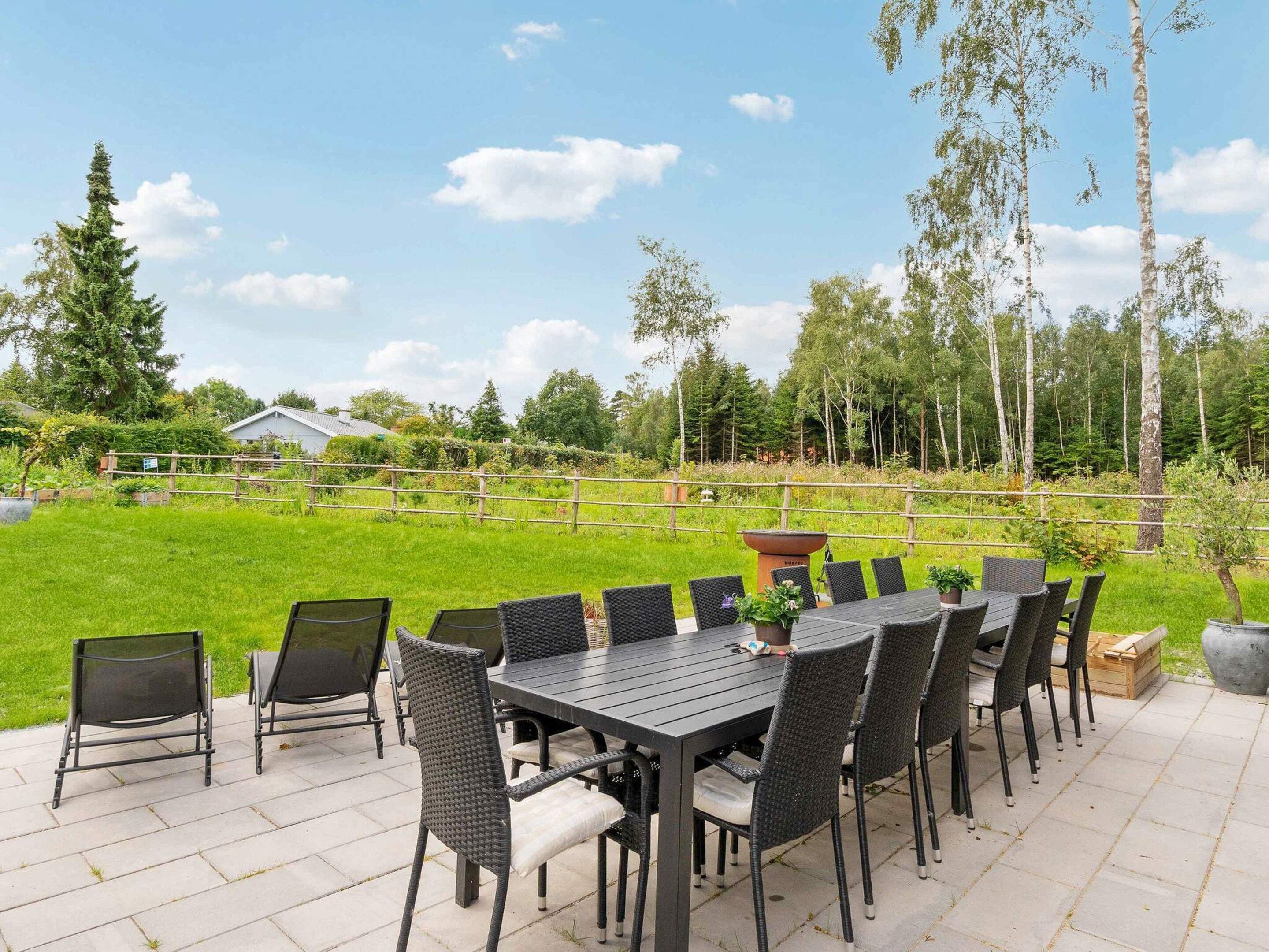 An outdoor patio with a table and chairs, surrounded by a grassy area and trees.