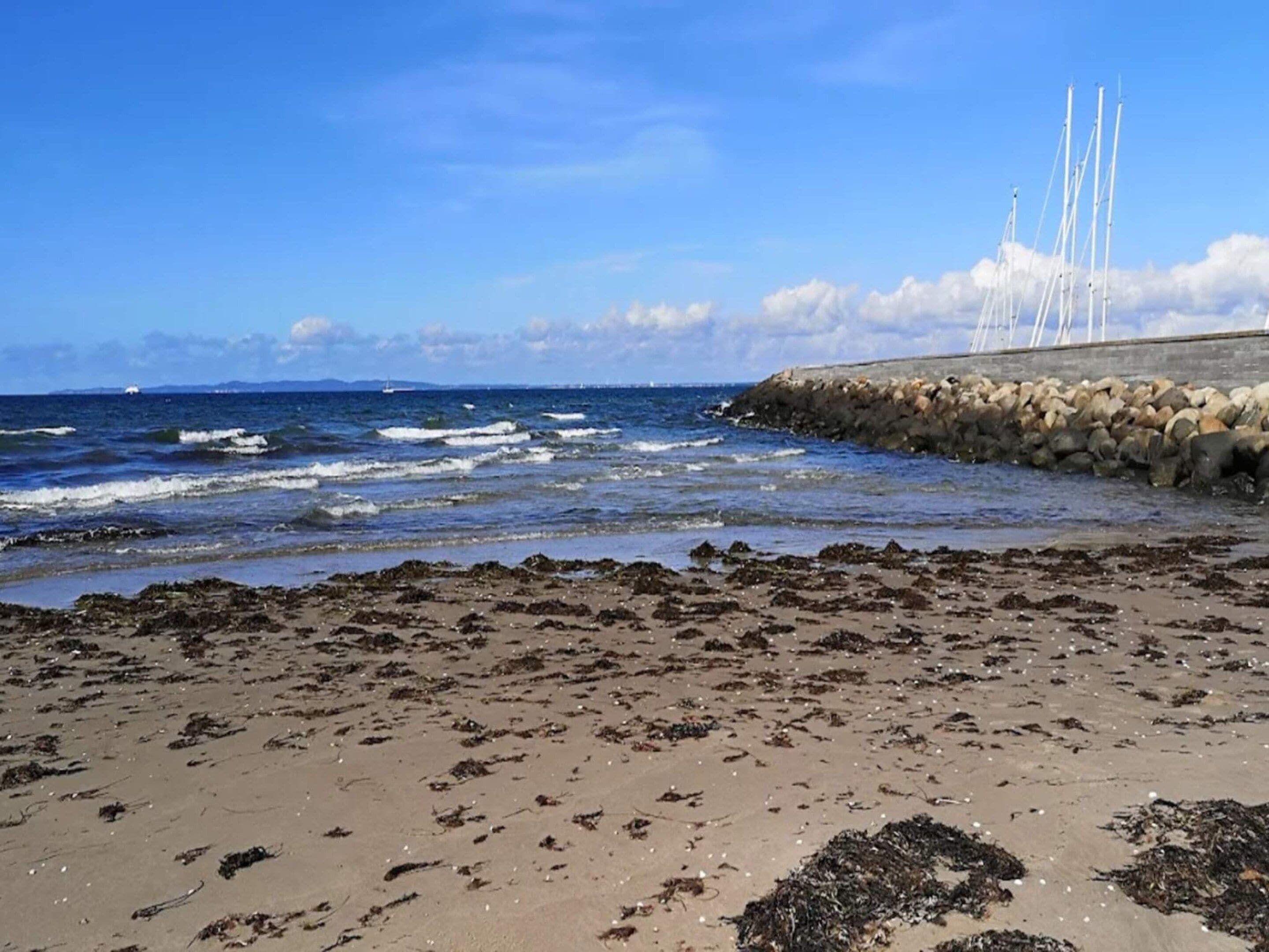 A beach with waves, a rocky breakwater, and a clear sky.
