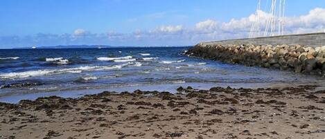 A beach with waves, a rocky breakwater, and a clear sky.