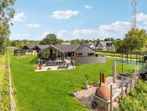 Een woonhuis met een ruime patio, tuinmeubels en een barbecue.