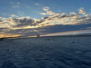 Een strand met een zonsondergang, twee mensen wandelend, en een horizon in de verte.