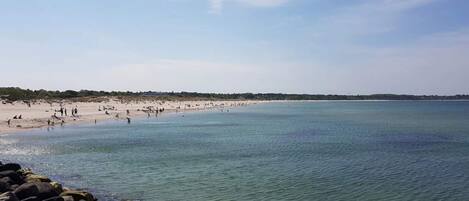 Una playa con agua cristalina, costa rocosa y árboles a lo lejos.
