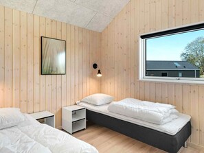 A room with wooden walls, a bed with white bedding, a bedside table, a small shelf, and a window with a view of a building. - 5 Star Holiday Home in Dronningmolle (Dronningmolle)