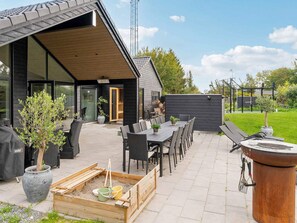 Een terras met buitenmeubilair, een barbecue en een houten speeltuintje.
