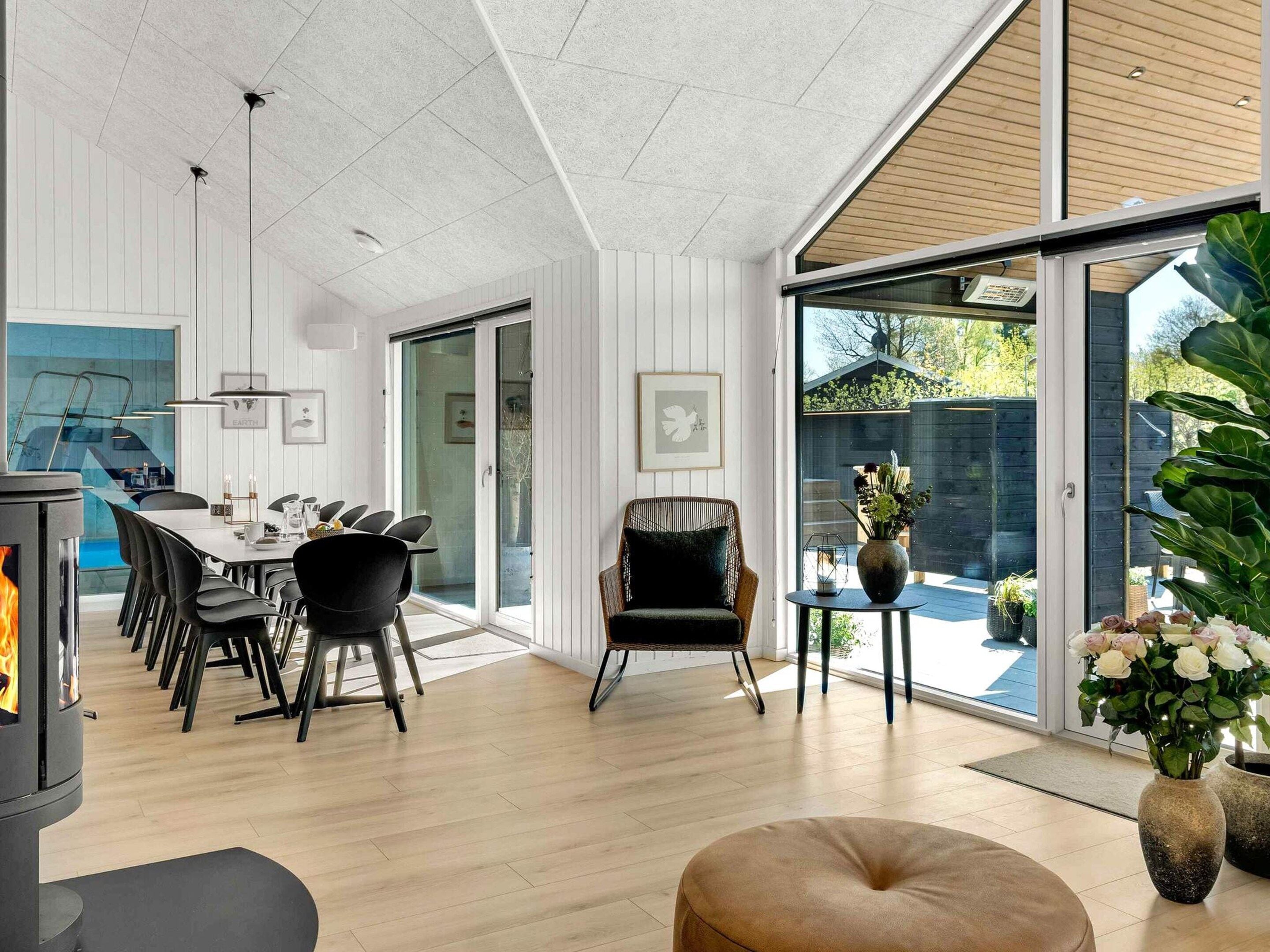 Ein modernes Interieur mit Essbereich, Kamin, einer Sitzecke mit Sessel und Tisch sowie Blick durch eine Glastür.