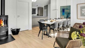 Een moderne keuken met een centraal eiland, een eetgedeelte met een tafel en stoelen, en een open haard met een vlam.