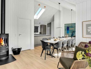 Een moderne keuken met een centraal eiland, een eetgedeelte met een tafel en stoelen, en een open haard met een vlam.