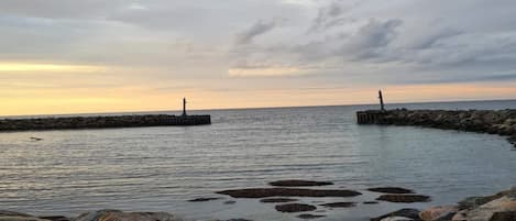 A coastal scene with a rocky shoreline, calm water, and two distant lighthouses.