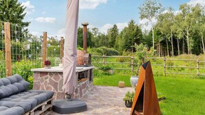 Een terras buiten met een stenen open haard, een overdekte barbecue en een zithoek met kussens.