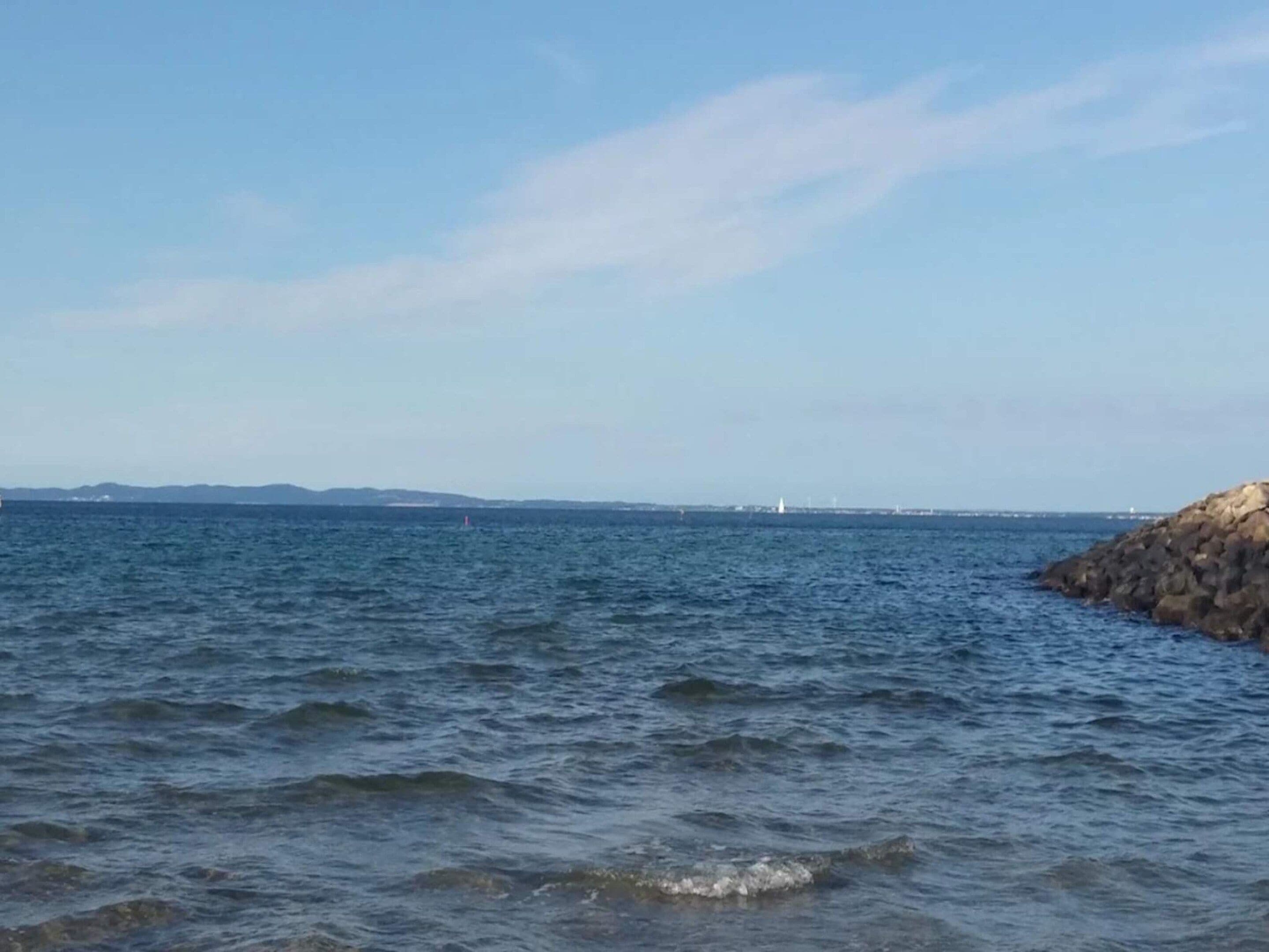 A coastal view with calm waters, a rocky outcrop, and distant landforms.