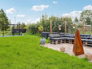 A backyard with a grassy lawn, a wooden deck, a metal fence, and a black shed. - 5 Star Holiday Home in Dronningmolle (Dronningmolle)