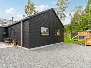A modern house with a dark exterior, a gravel driveway, a patio with outdoor furniture, and a wooden deck. - 5 Star Holiday Home in Dronningmolle (Dronningmolle)