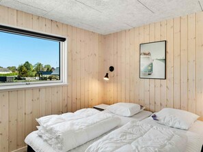 A bedroom with a wooden paneled wall, a bed with white bedding, a window with a view of greenery, and a wall-mounted lamp. - 5 Star Holiday Home in Dronningmolle (Dronningmolle)