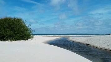 A beach with white sand, a narrow water channel, and a clear blue sky.