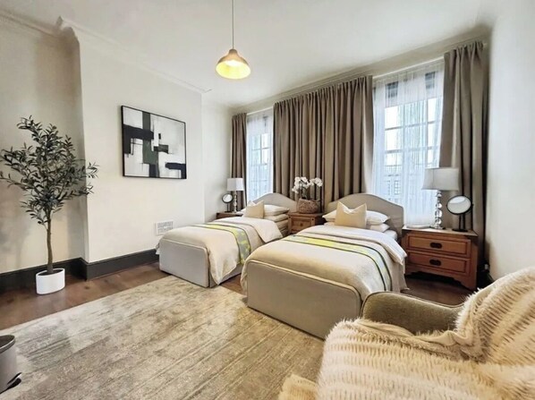 A hotel room with two beds, a large window with curtains, a potted plant, and a hanging light fixture.