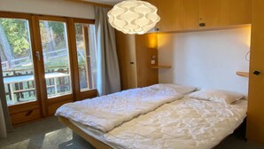 A bedroom with a bed, wooden walls, a pendant light, and a view through a glass door. - Radiant Apartment Facing Hills (Veysonnaz)