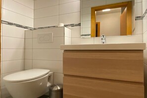 A bathroom with a toilet, a sink with a mirror, and a trash bin. - Radiant Apartment Facing Hills (Veysonnaz)