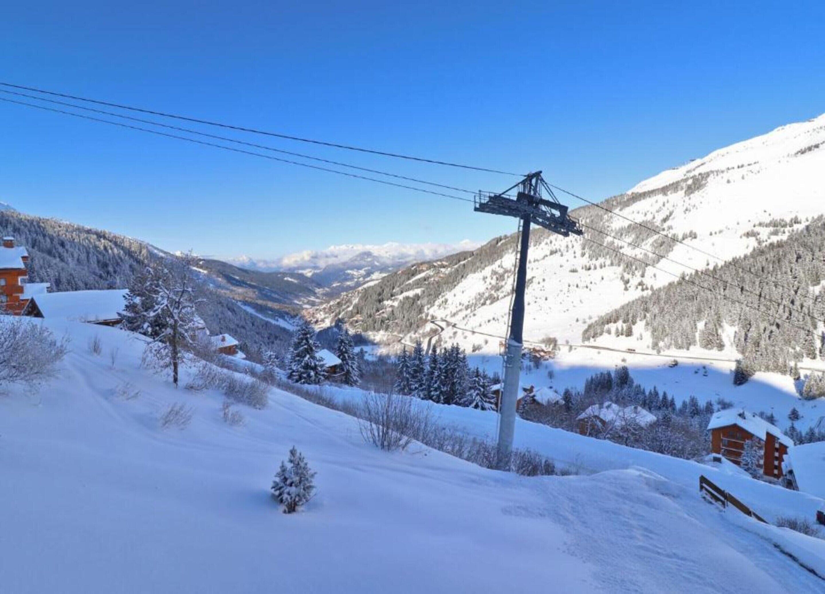 A snow-covered mountain landscape with a ski lift, buildings, and a clear blue sky.