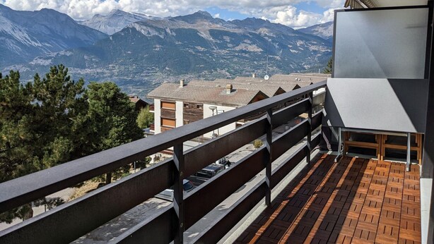 Ein Balkon mit Blick auf Berge, Holzboden und Metallgeländer.
