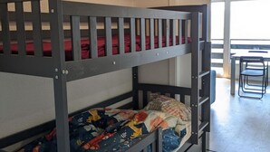 Ein Stockbett mit roter und blauer Bettwäsche, ein kleiner Tisch und ein Stuhl in einem Zimmer mit Fenster.