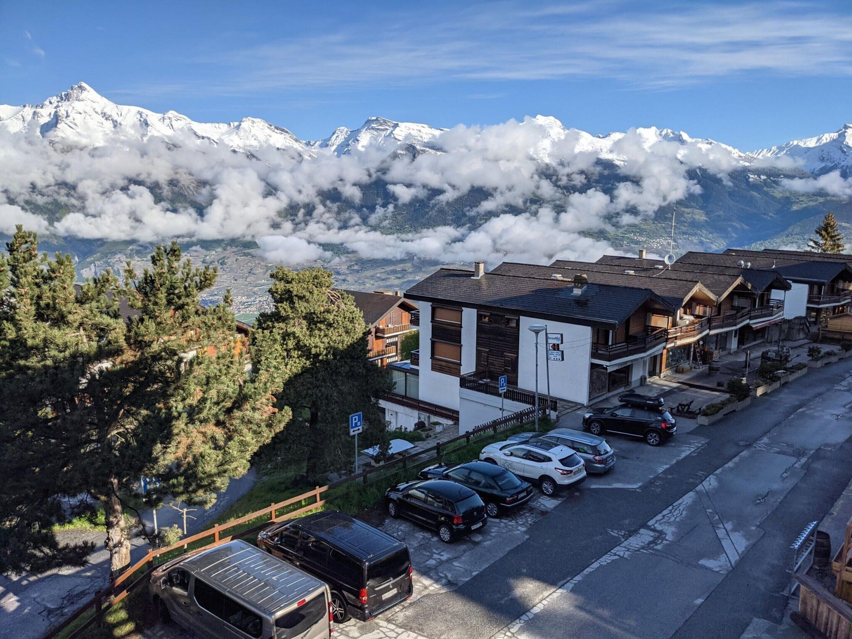 A mountain resort with snow-capped peaks, a parking area, and traditional wooden buildings.