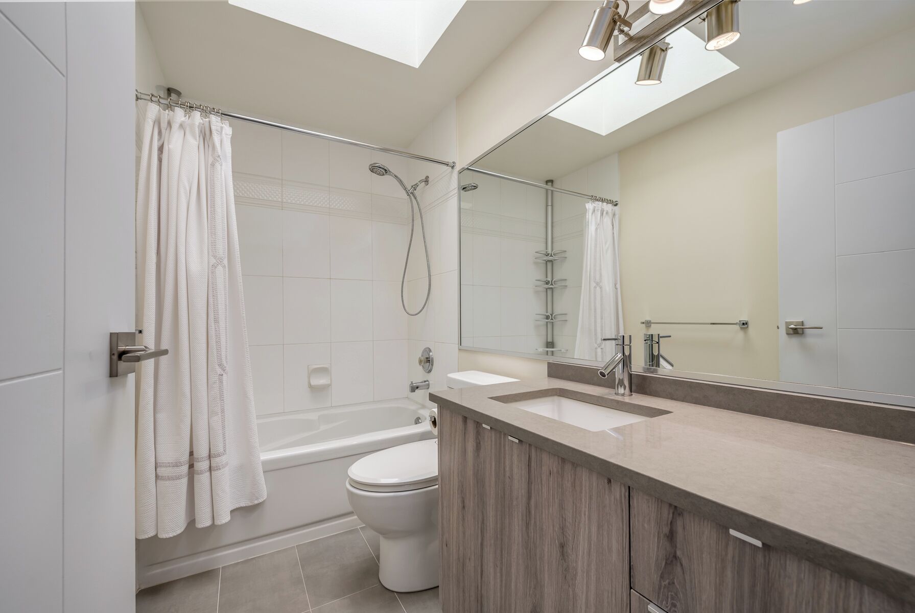 A modern bathroom with a glass shower enclosure, a freestanding bathtub, a toilet, and a vanity with a mirror.