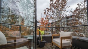A balcony with a wooden floor, a glass door, a potted plant, and a cushioned chair. - Live the North Shore dream in this mountain-view penthouse! (North Vancouver)