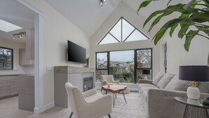 A spacious living area with a fireplace, a television mounted on the wall, and a large window offering a view of the city. - Live the North Shore dream in this mountain-view penthouse! (North Vancouver)