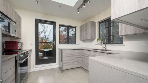 A modern kitchen with a skylight, built-in appliances, and a view of the outdoors. - Live the North Shore dream in this mountain-view penthouse! (North Vancouver)