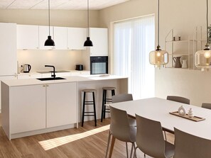 A modern kitchen with white cabinets, a central island, black pendant lights, and a dining area with a white table and chairs. - 5 Star Holiday Home in Vestervig (Vestervig)