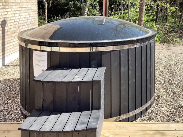 A hot tub with a wooden deck and steps leading up to it, surrounded by gravel and trees. - 5 Star Holiday Home in Vestervig (Vestervig)
