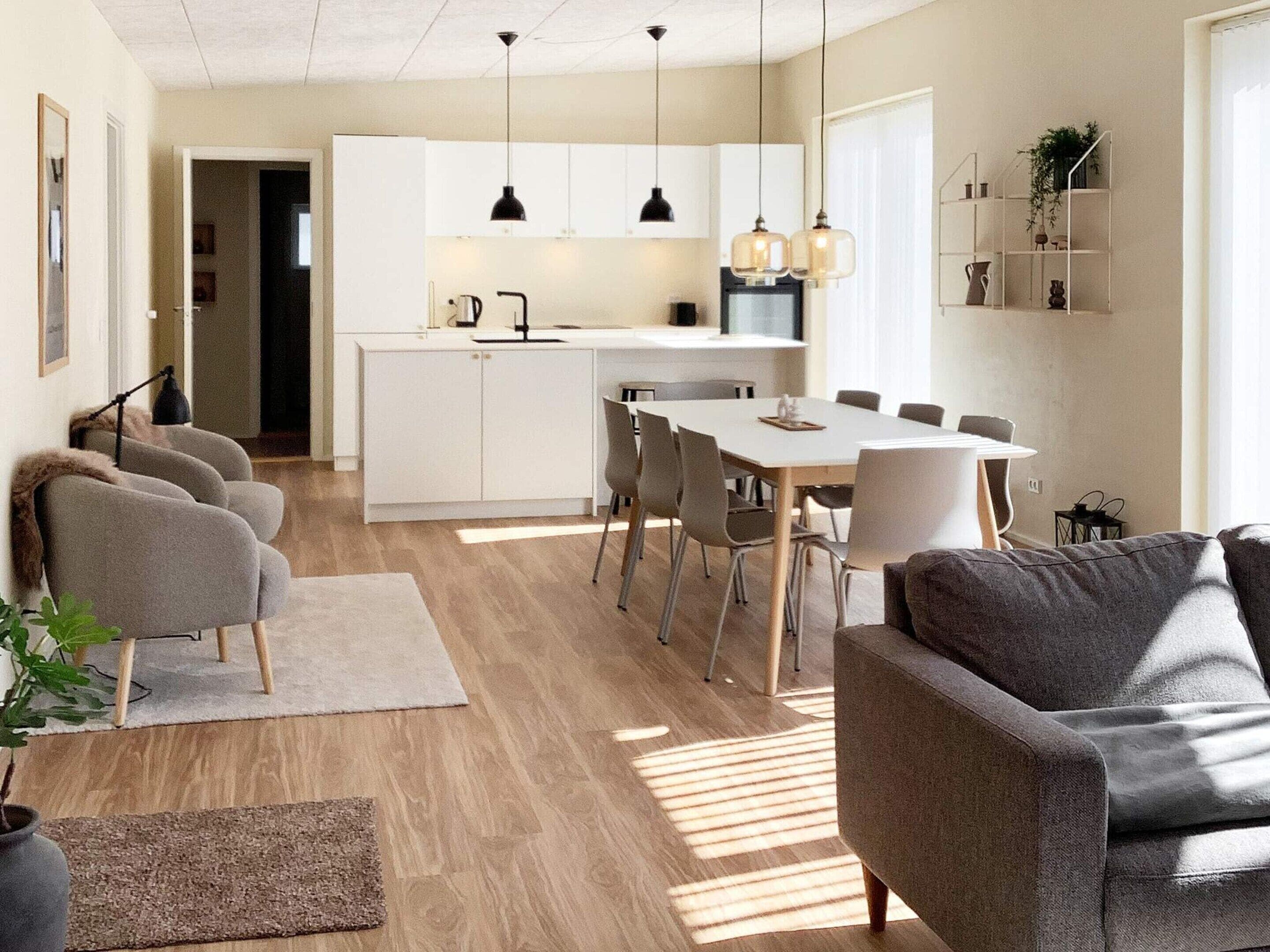 A modern kitchen with white cabinetry, a central island, pendant lighting, and a dining area with a white table and chairs.