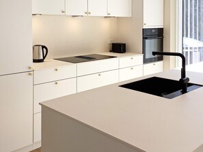 Una cocina moderna con armarios blancos, un lavamanos negro y un horno empotrado.