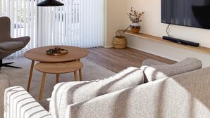 A modern living room with a round wooden coffee table, a sofa, a television mounted on the wall, and a window with vertical blinds. - 5 Star Holiday Home in Vestervig (Vestervig)