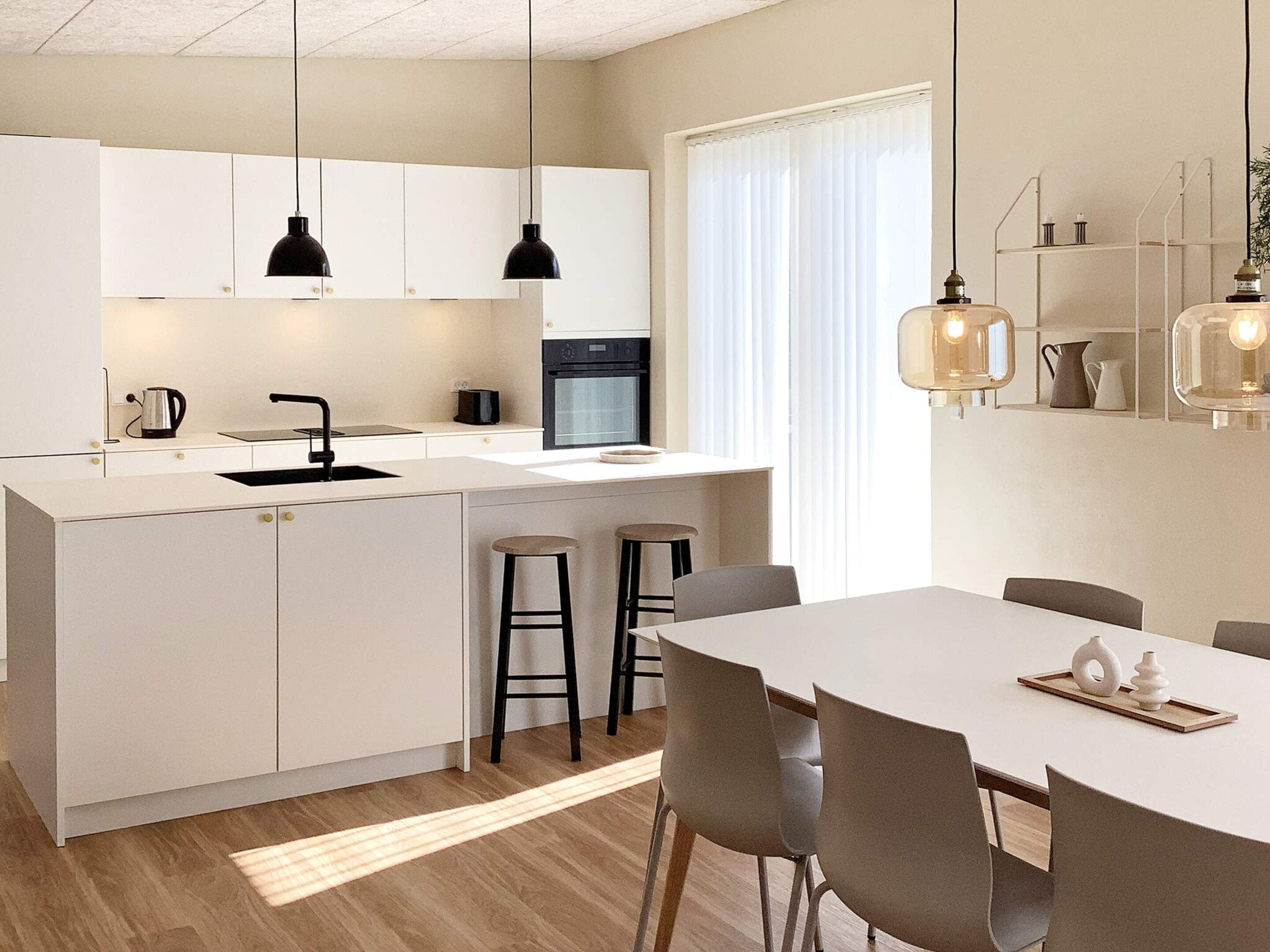 A modern kitchen with white cabinetry, a central island, bar stools, and pendant lighting.