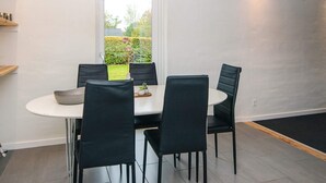 Een eetgedeelte met een ronde tafel, vier stoelen, een hanglamp en uitzicht op een tuin door een deur.