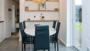 A dining area with a round table, four chairs, a hanging light fixture, and a view through a glass door to the outside. - 6 Person Holiday Home in Ansager (Ansager)