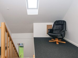 Ein Eckzimmer mit einem schwarzen Ledersessel, einem Oberlicht und einer Holztreppe.