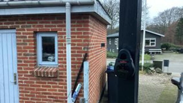 A brick building with a window, a door, and a black object attached to the wall. - 6 Person Holiday Home in Ansager (Ansager)