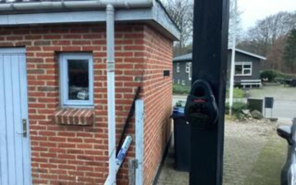 A brick building with a window, a door, and a black object attached to the wall. - 6 Person Holiday Home in Ansager (Ansager)