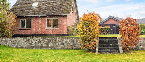 A brick house with a tiled roof, a stone wall, and a grassy yard.
