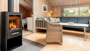 Interior acogedor de una cabaña con estufa de leña, un sofá y una silla de mimbre.